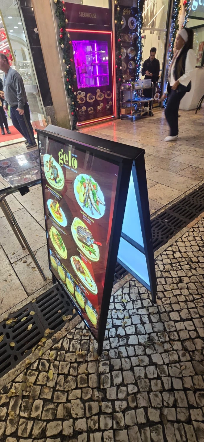 Illuminated A-board with restaurant menu graphic outside a shop